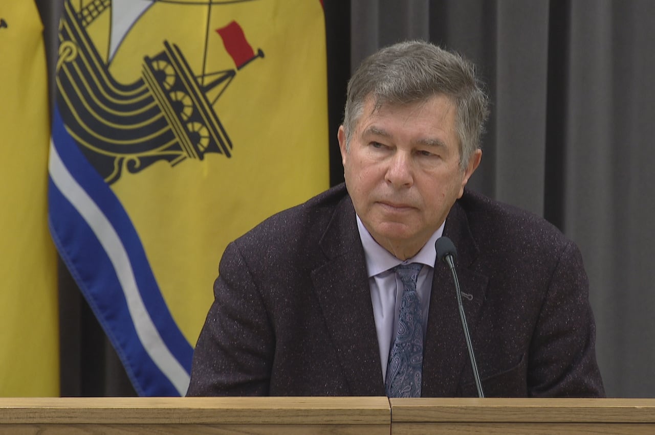Man in a suit with grey hair sitting at a mic during a press conference.