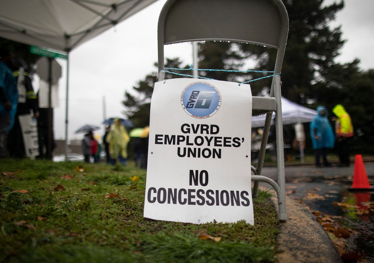 A sign says 'GVRD Employees' Union No Concessions' on grassy ground during a rainy day.