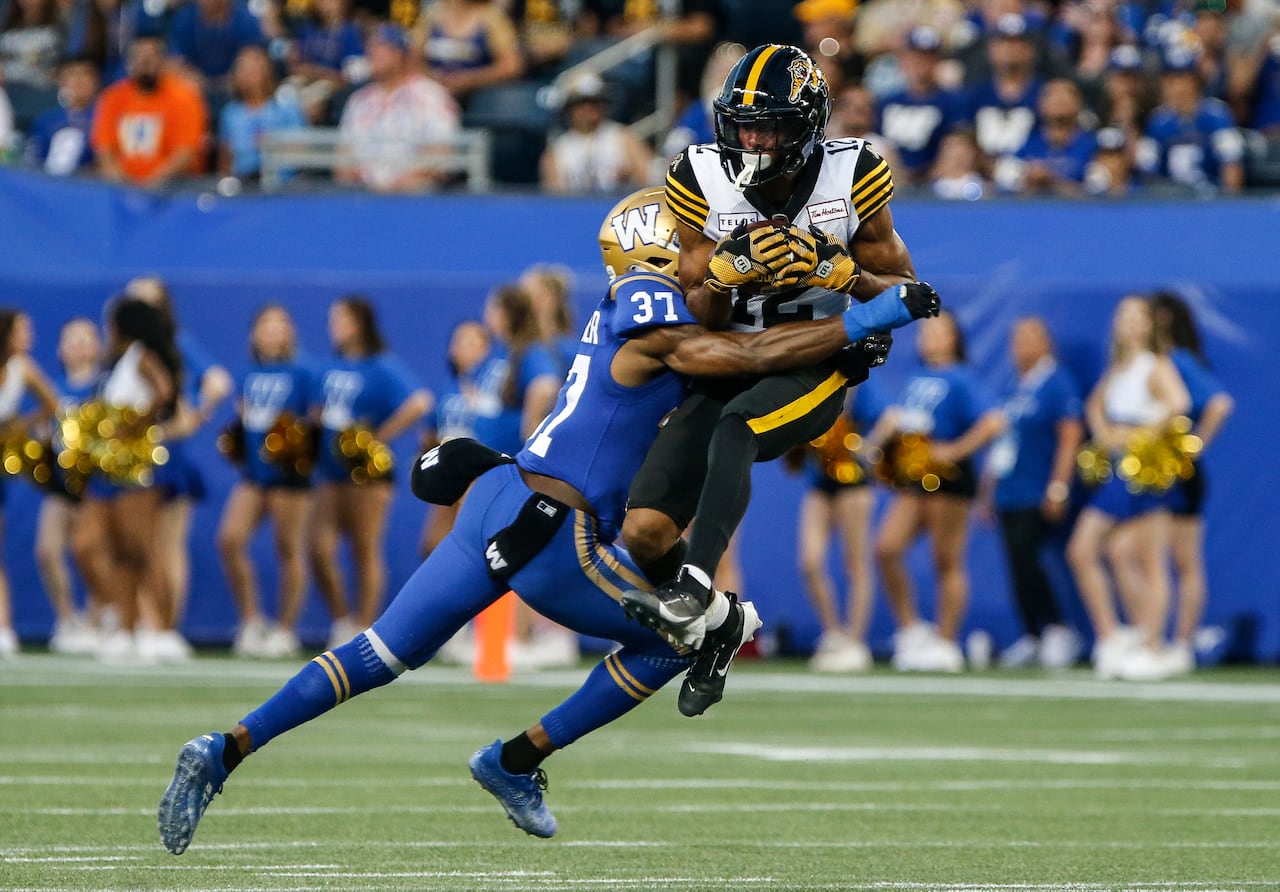 A football player in black and yellow leaps up to make a catch as he's hit by an opposing player in blue and gold.