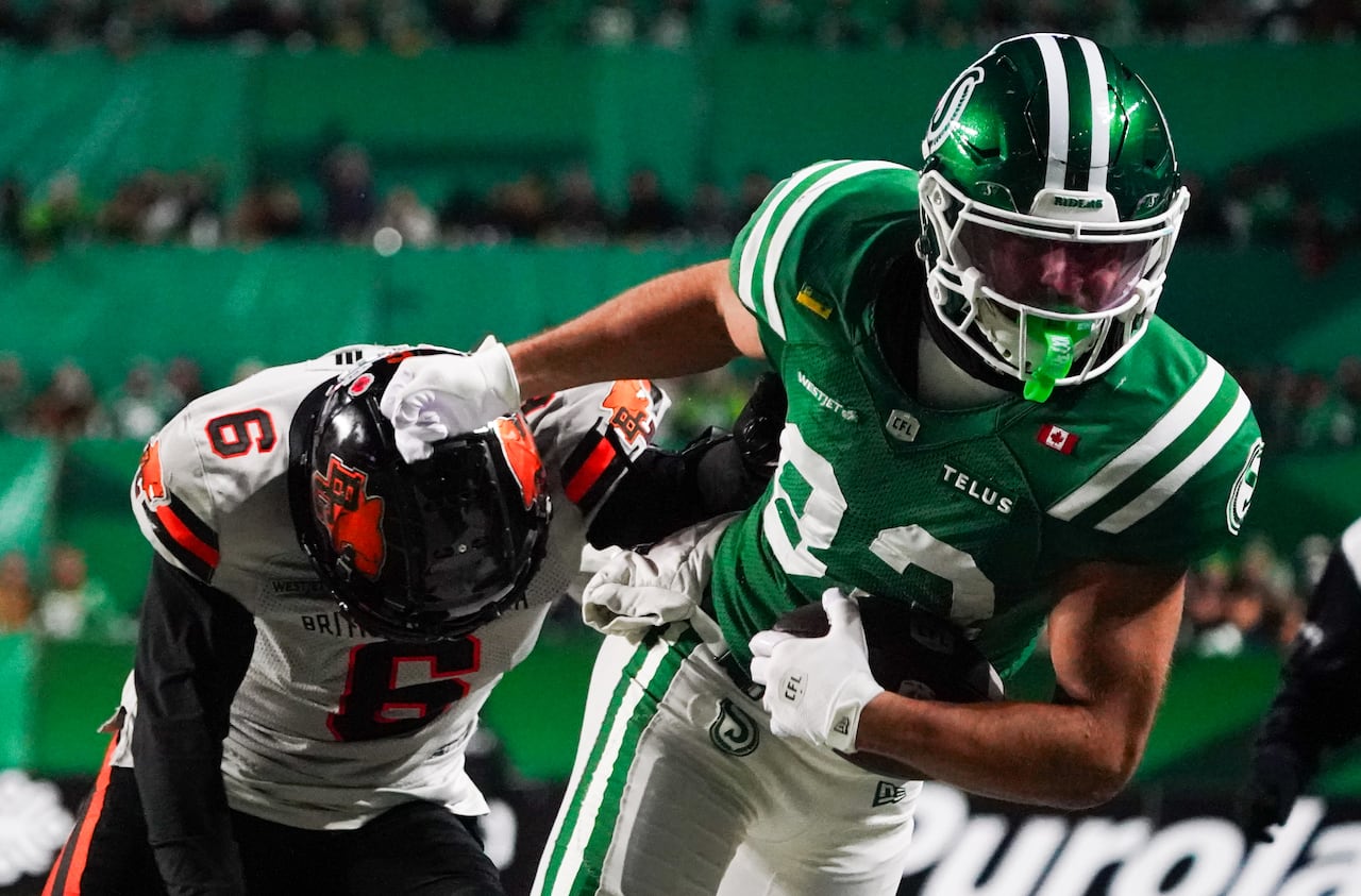 A football player in green and white pushes away an opposing player in orange and black.