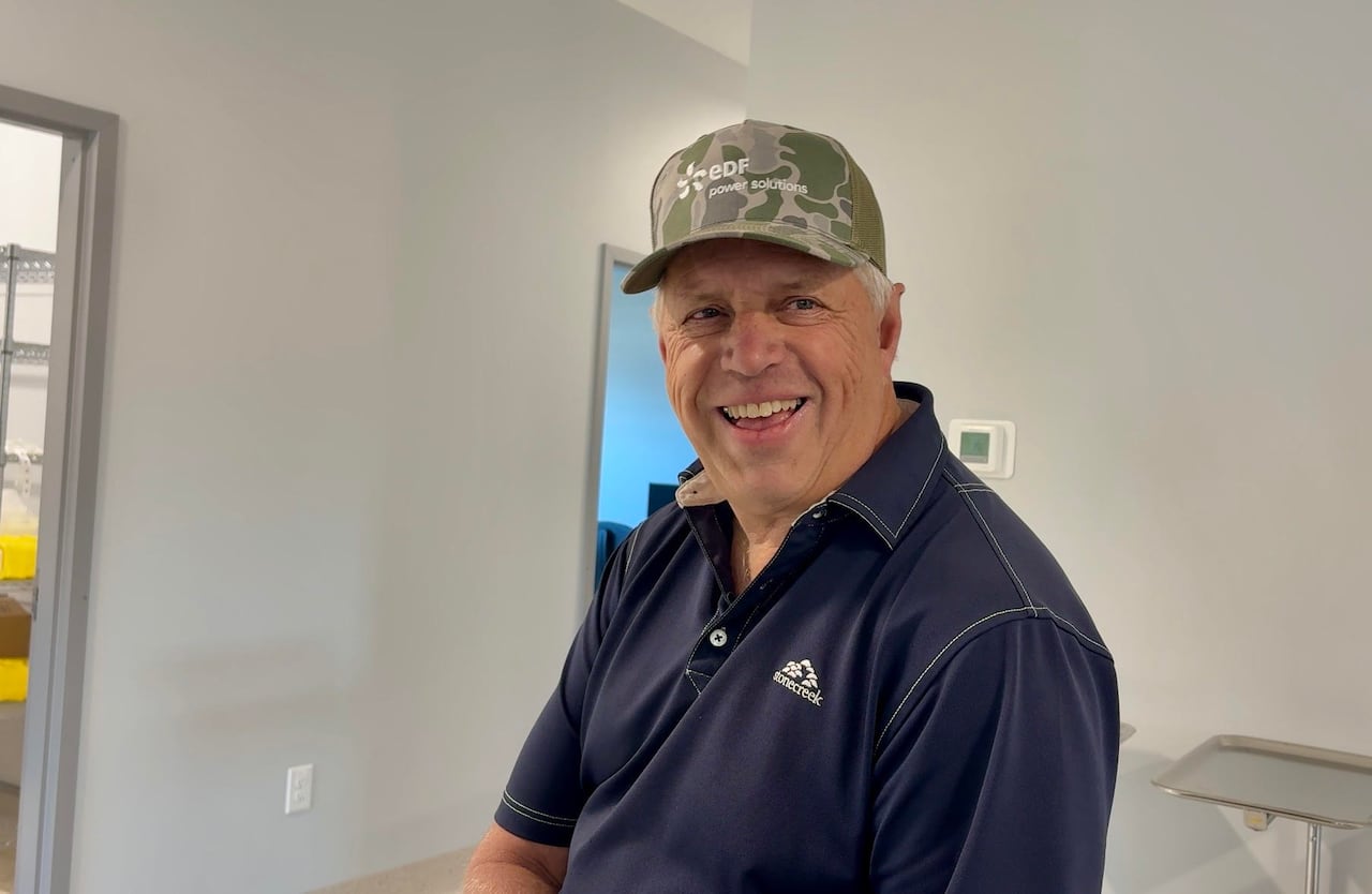 A man wearing a cap and a blue short-sleeved shirt is smiling