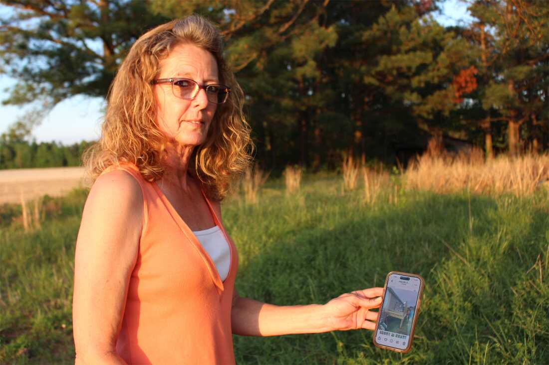 Debra Pierce stands in grassy field holding a phone to show the photographer a picture on the screen.