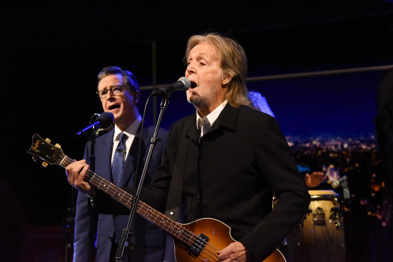 Two men sing on a stage. One man plays the guitar.