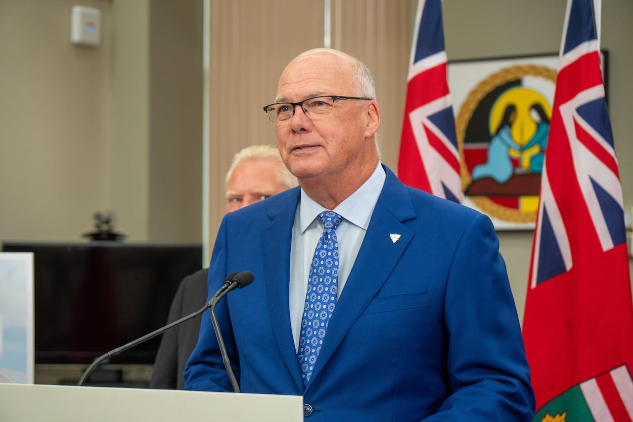 A person is seen standing at a podium speaking into a microphone. They are wearing a blue suit.