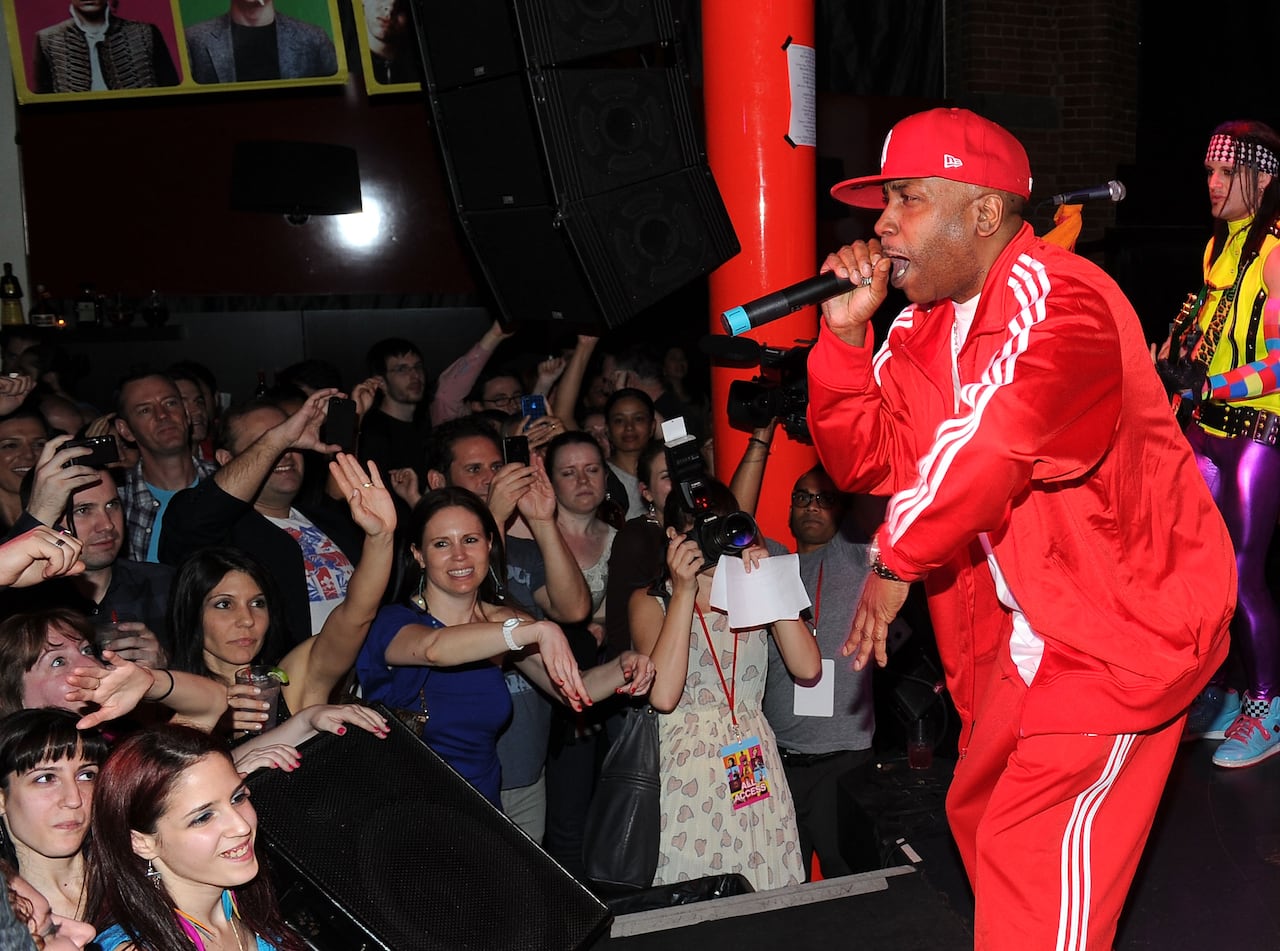 A man in a red adidas track suit wraps into a microphone on stage in front of a large crowd