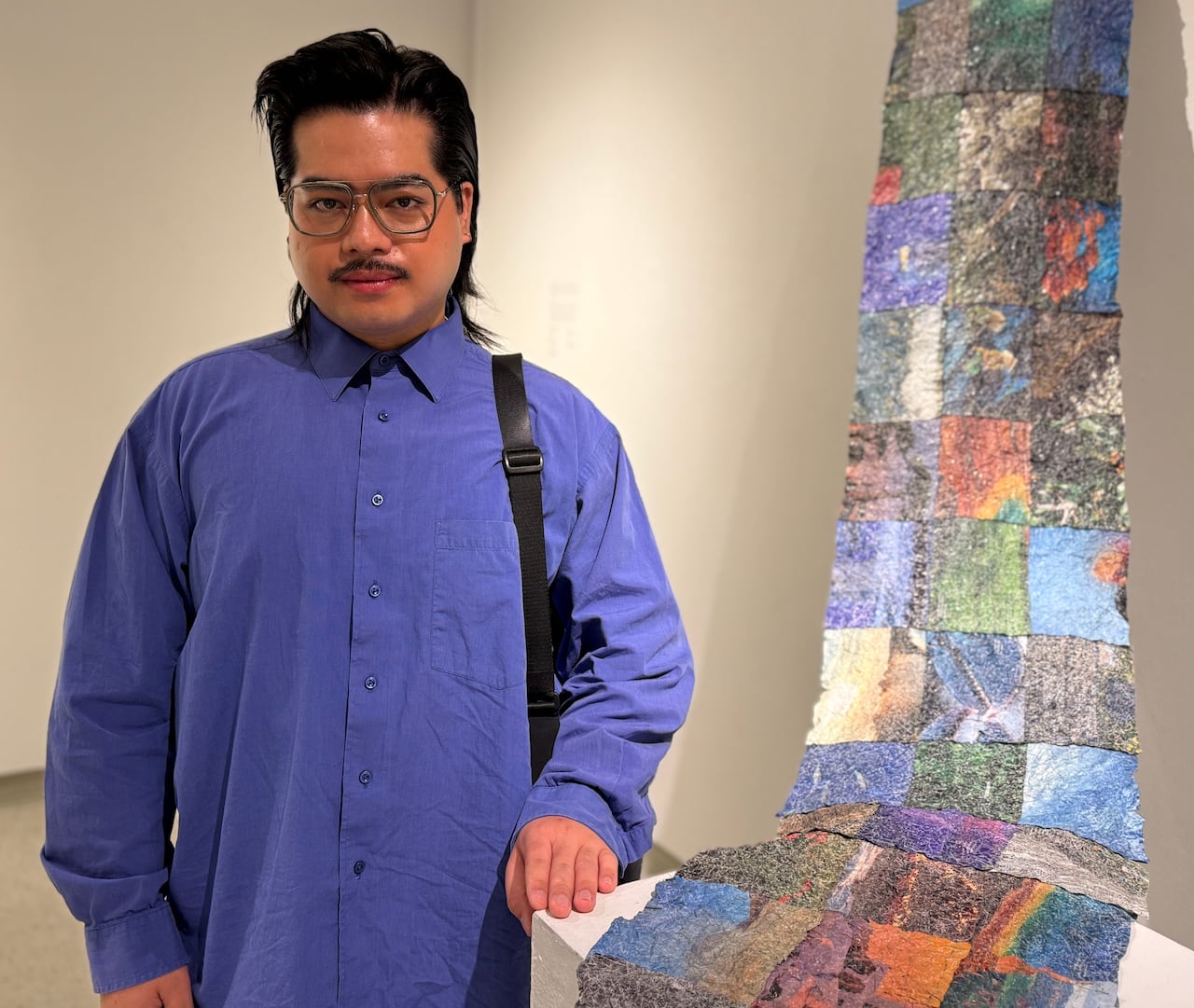 A man standing next to an artwork made of squares that flows down from a wall and over a small table.