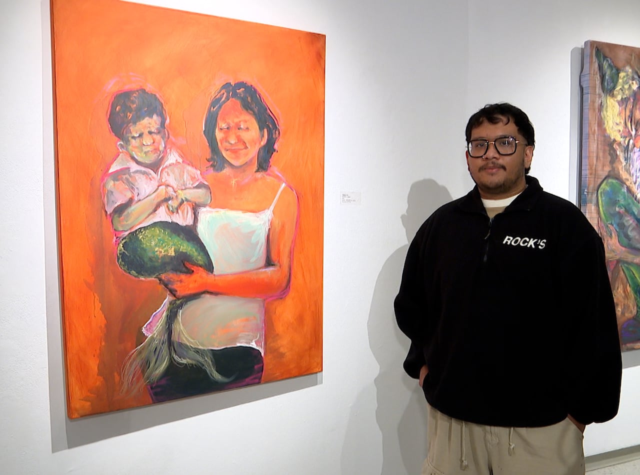 A man stands in a gallery next to a colourful oil painting.