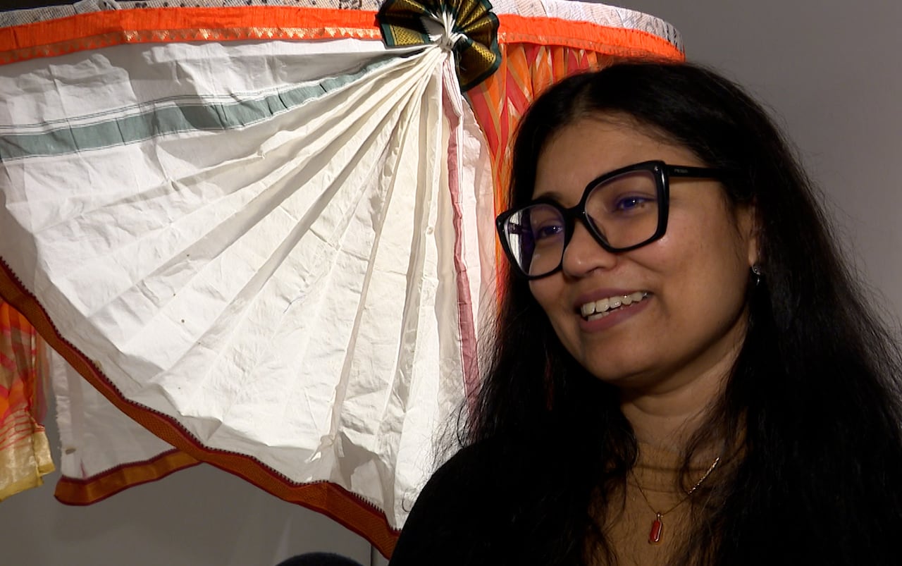 A woman stands next to a fan-like artwork made of folded fabric.