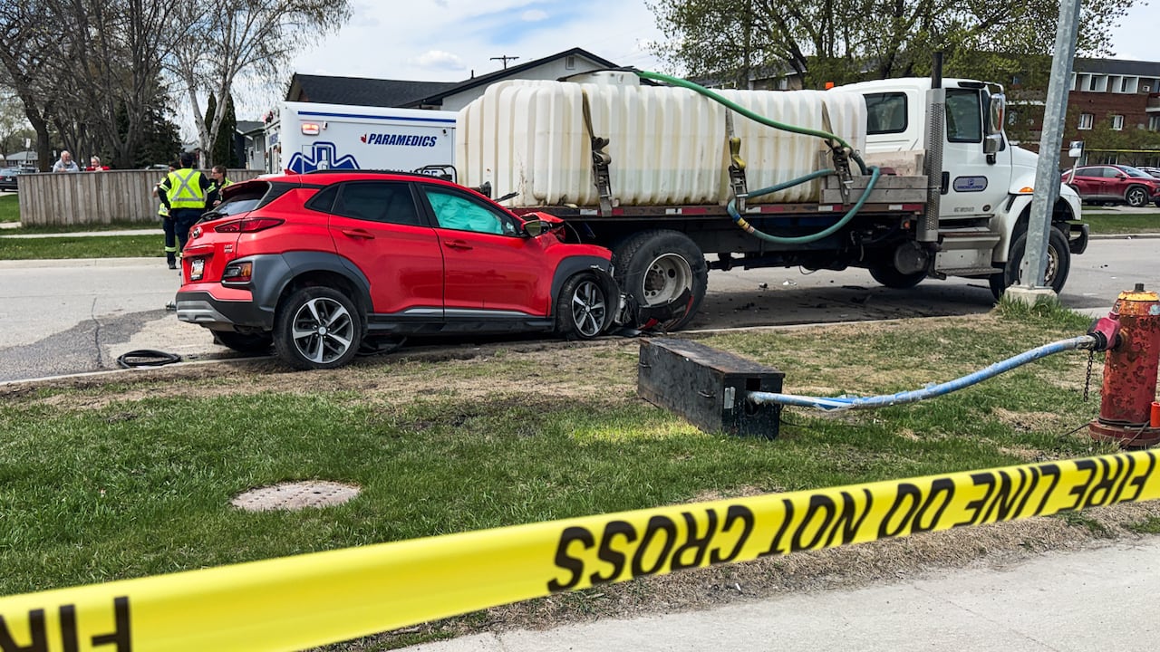 A red SUV is shown crumpled into the back of a water truck. Yellow caution tape is shown in the foreground and a paramedic vehicle with first responders are shown in the background
