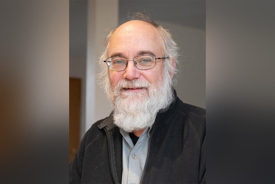 A man with a white beard and balding white hair smiles in a portrait photo.
