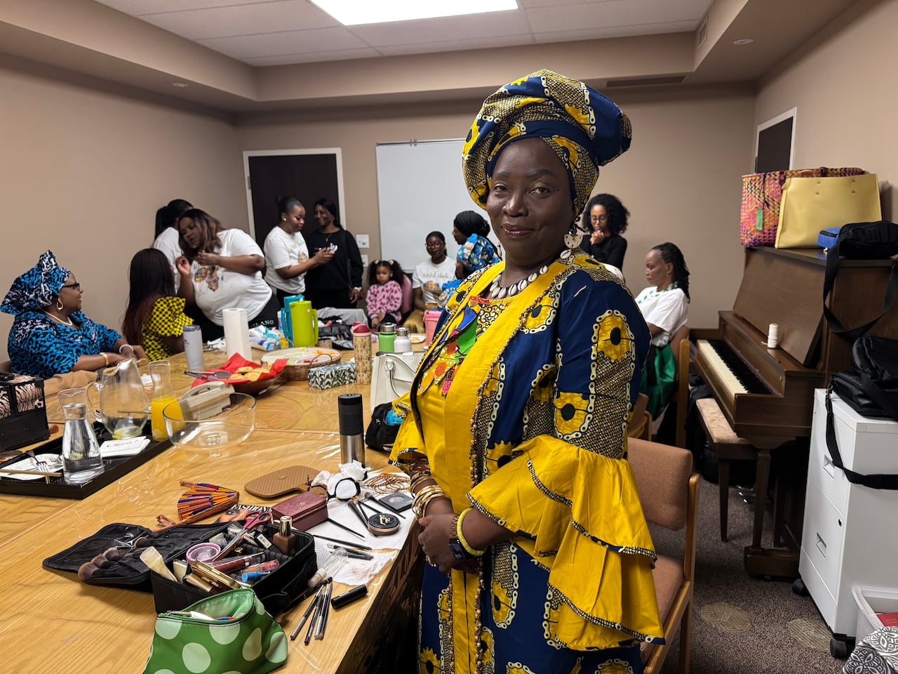 A woman wearing bright, colourful clothes besides a large table. There are several people in the background.