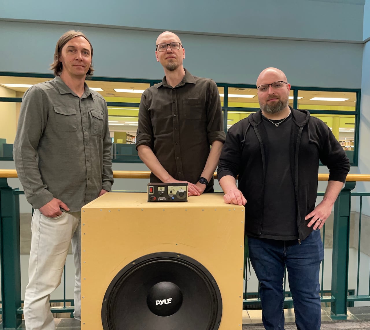 Three men stand behind a large speaker.