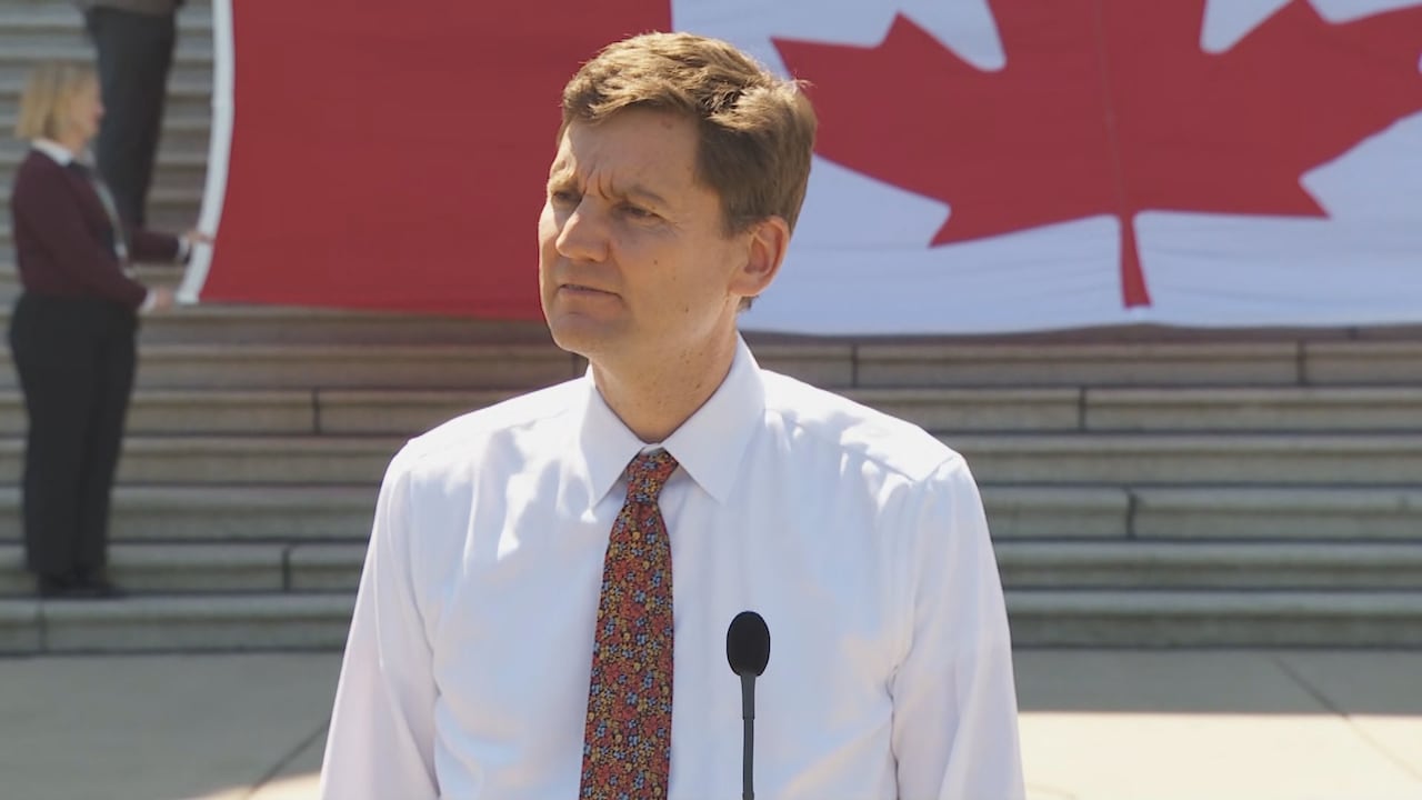 David Eby stands at a microphone in front of a very large Canadian flag