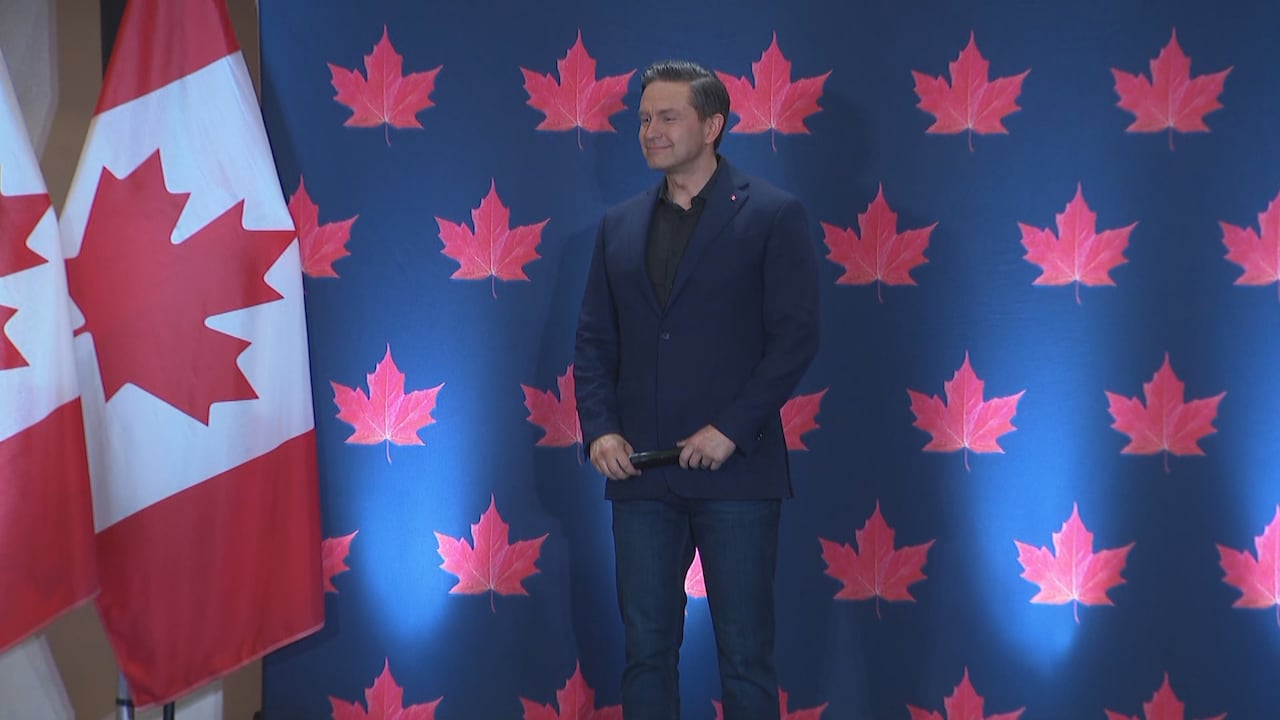 A man stands on a stage in front of a blue backdrop with red maple leaves and Canadian flags.