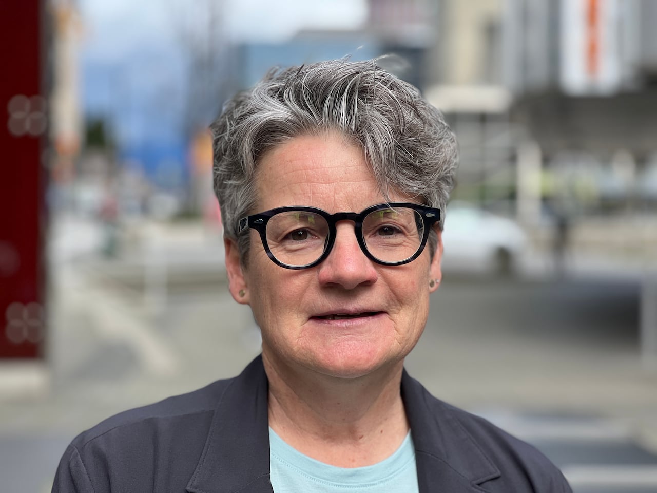 A woman in black glasses with short grey hair looks stands in Vancouver.