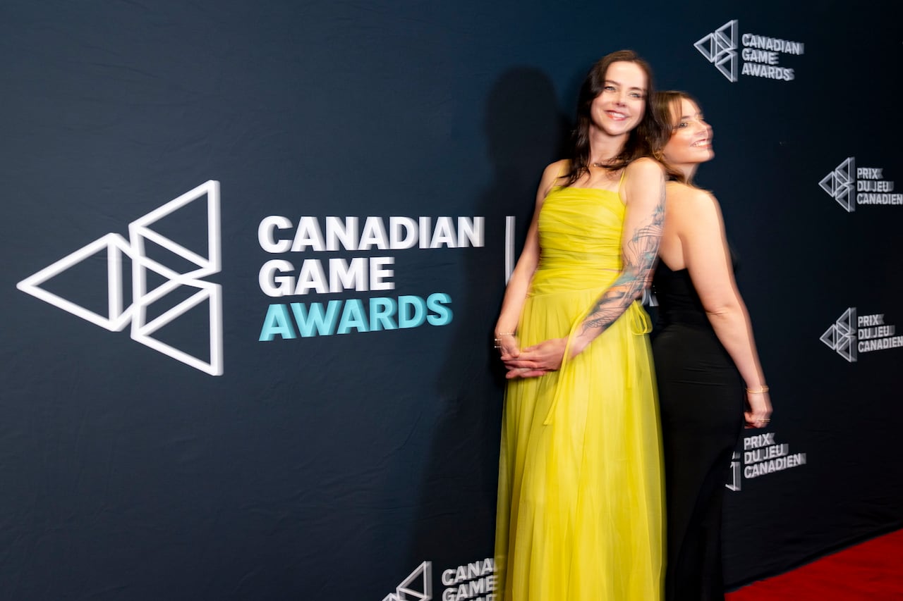 Two women in dresses pose on a red carpet in front of a wall for the Canadian Game Awards.
