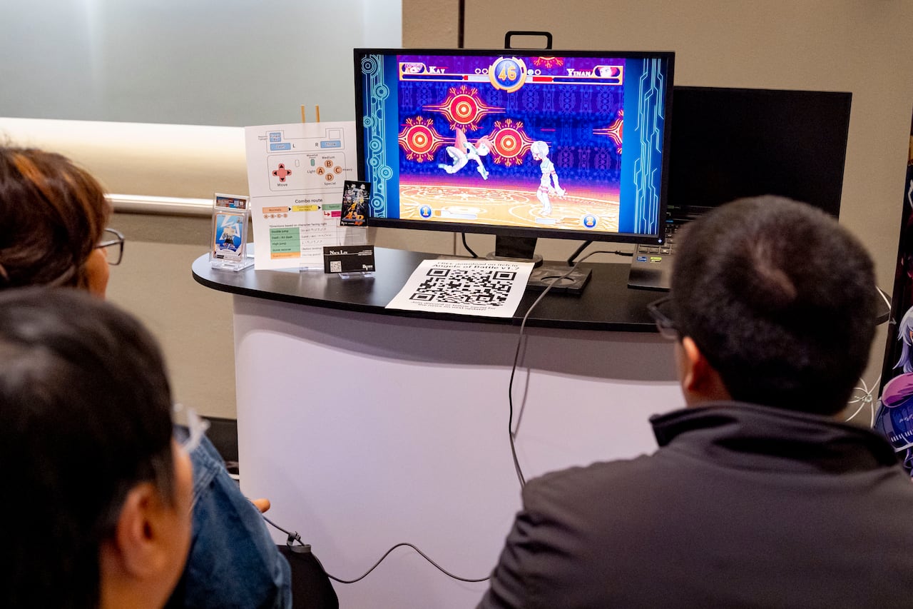 People are seated playing a video game at a kiosk.