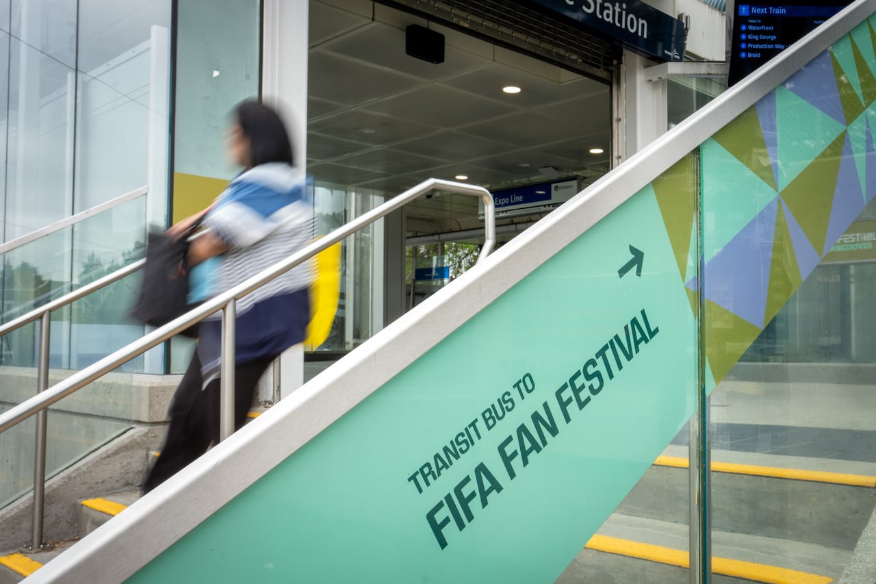 A person passes by a staircase with an advertising hoarding for the 'Transit bus to FIFA Fan Festival'.