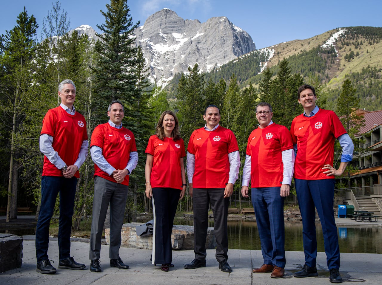Five men and one woman pose for photos wearing matching red T-shirts in a mountain setting