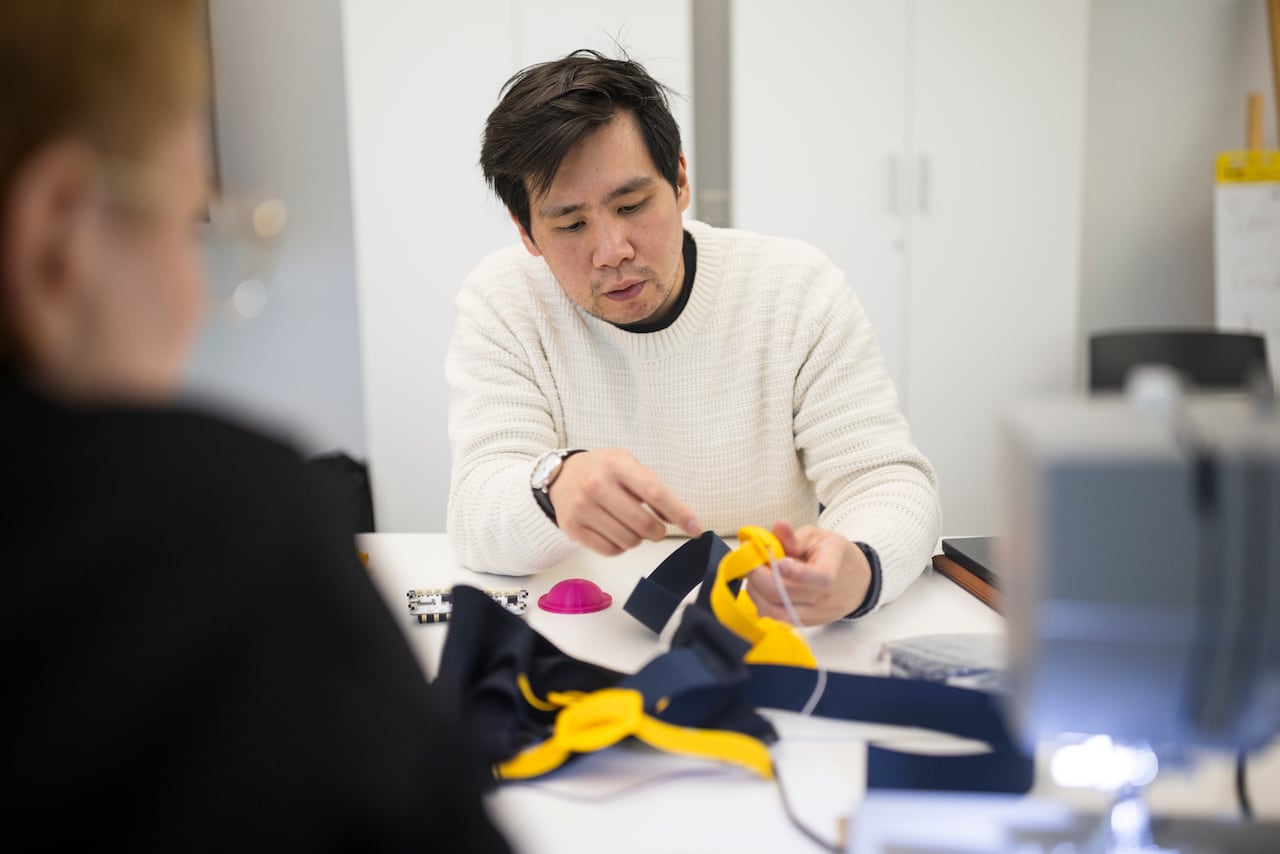 A man sits at a table and works on a harness vest device.