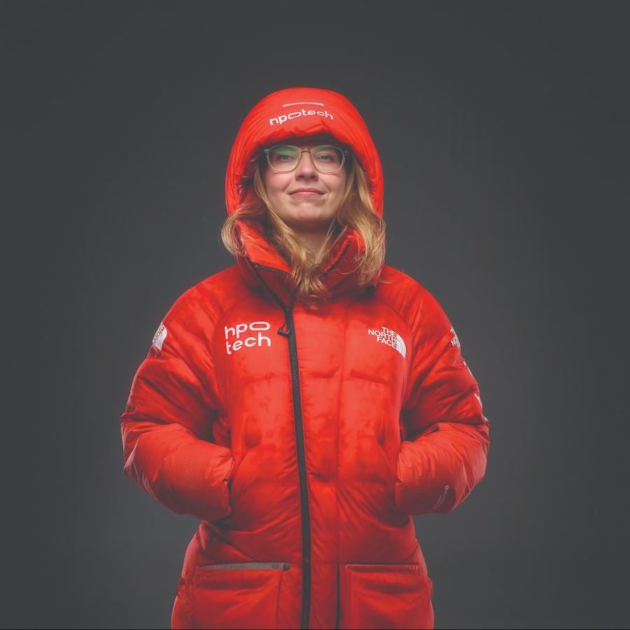 A woman poses for a photo, wearing a red puffer parka with her hood up.