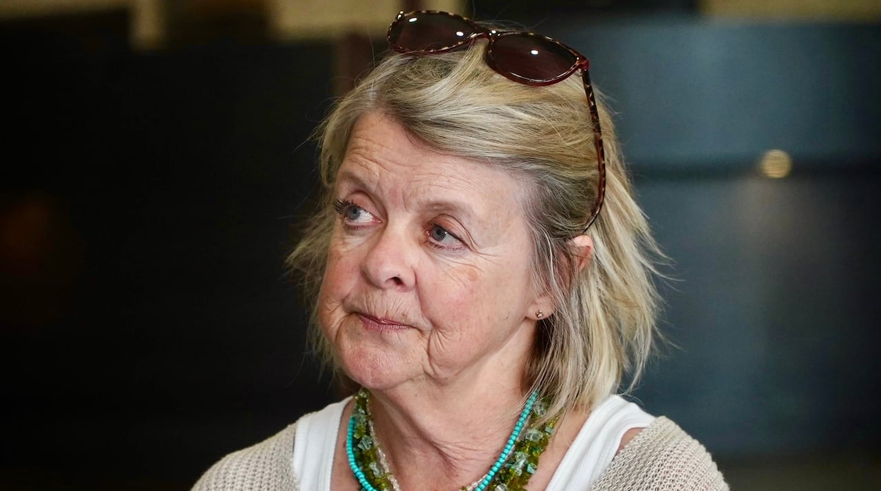 Woman with blonde hair wears sunglasses atop her head and wears a stack of green and blue necklaces