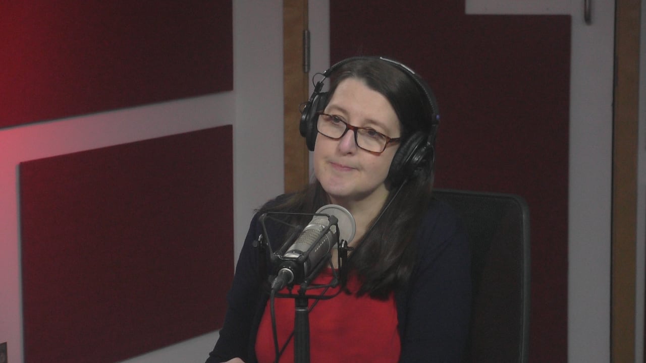 A woman with brown hair and glasses sits behind a radio microphone in the CBC studio.