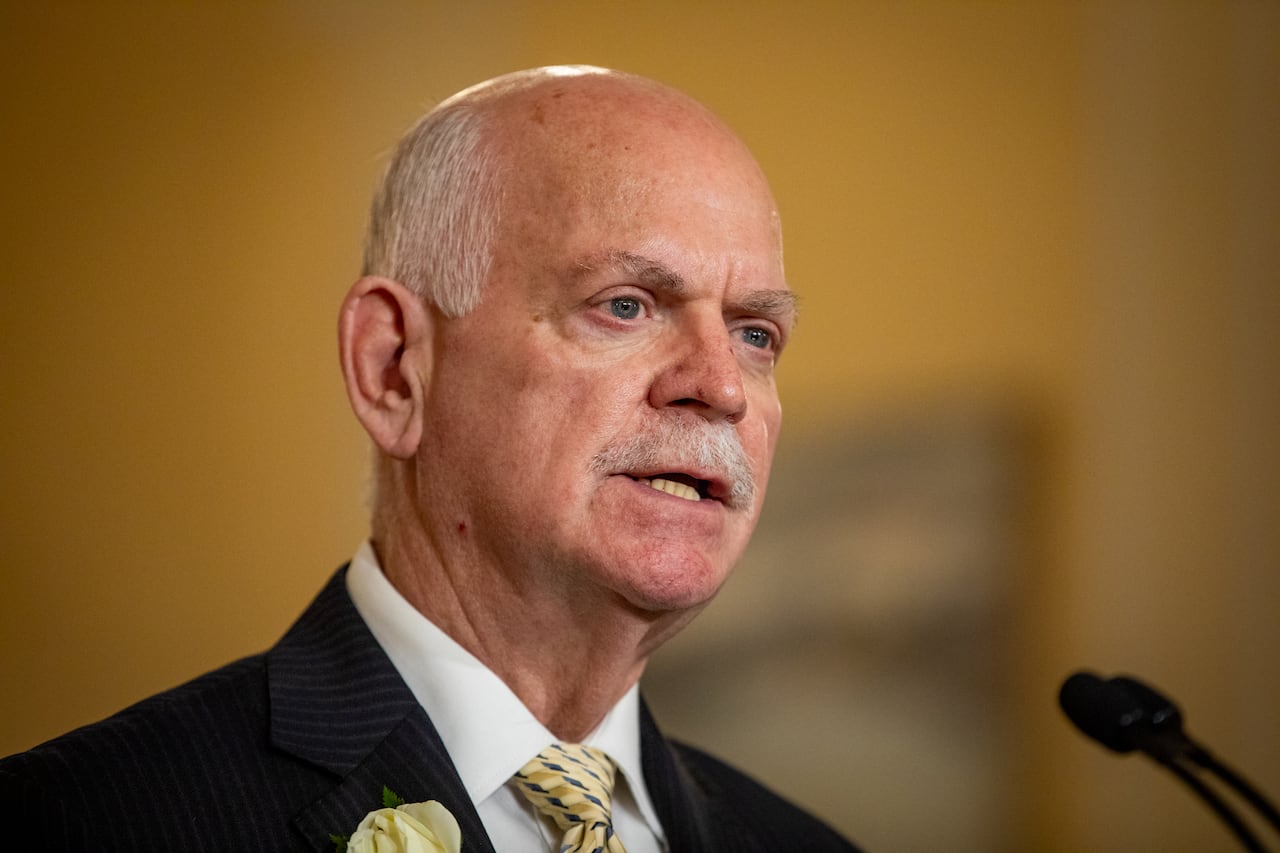 A man with balding white hair speaks into a mic.