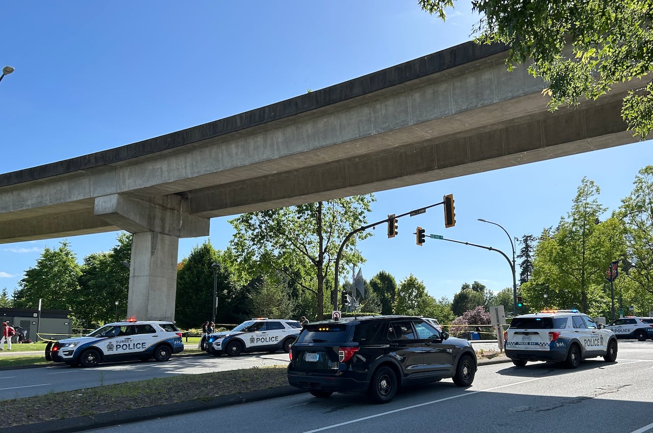 A number of parked police cars along a SkyTrain track and a park on a sunny day.