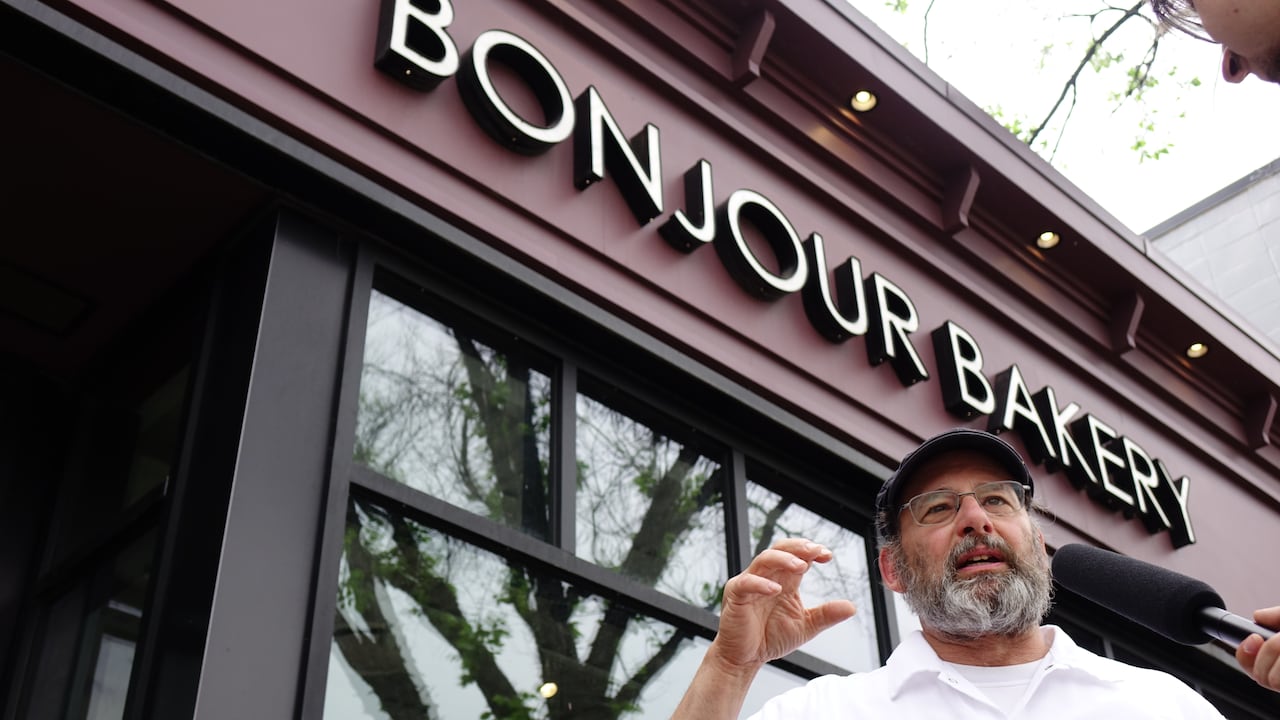 Man with white beard in front of a bakery.