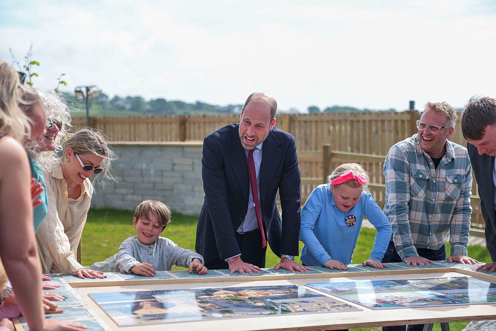 An adult and two children hold their hands out on a table as other people look on.