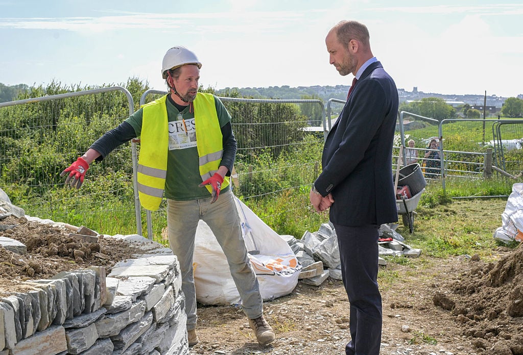 A person points to a stone wall being built as they talk to another person.