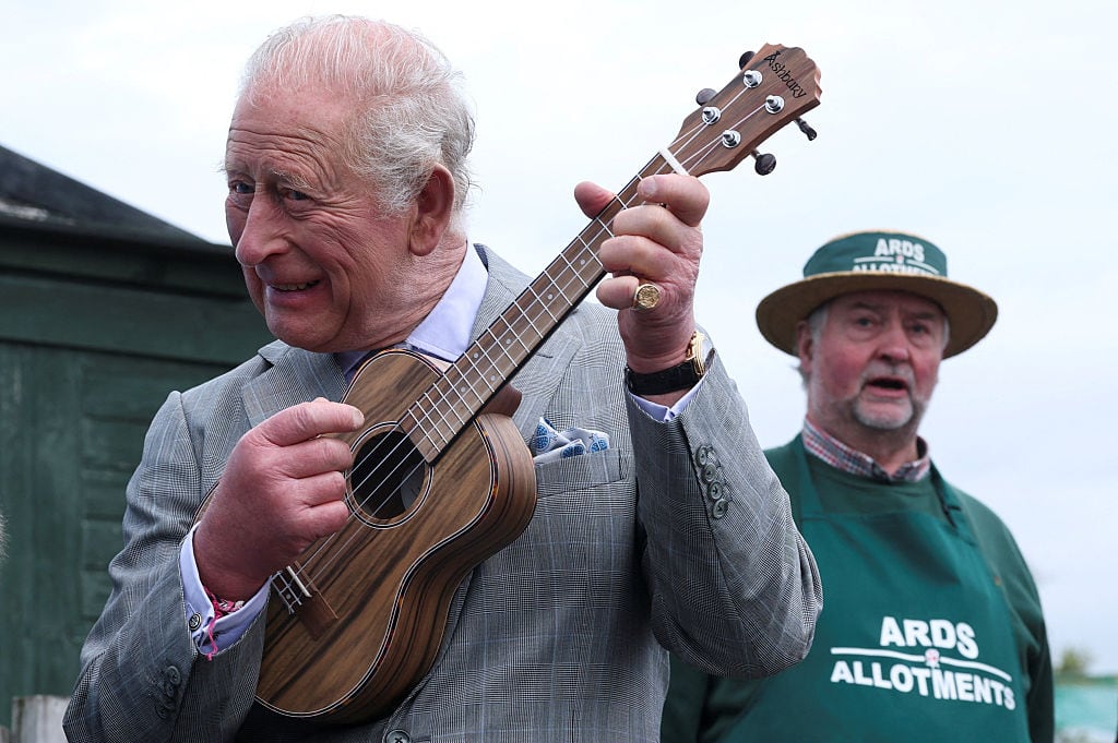 A person plays a ukelele as another person looks on.