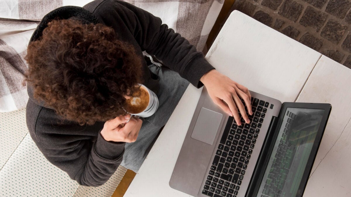 A photo from above showing a person holding a cup of coffee while typing on a laptop