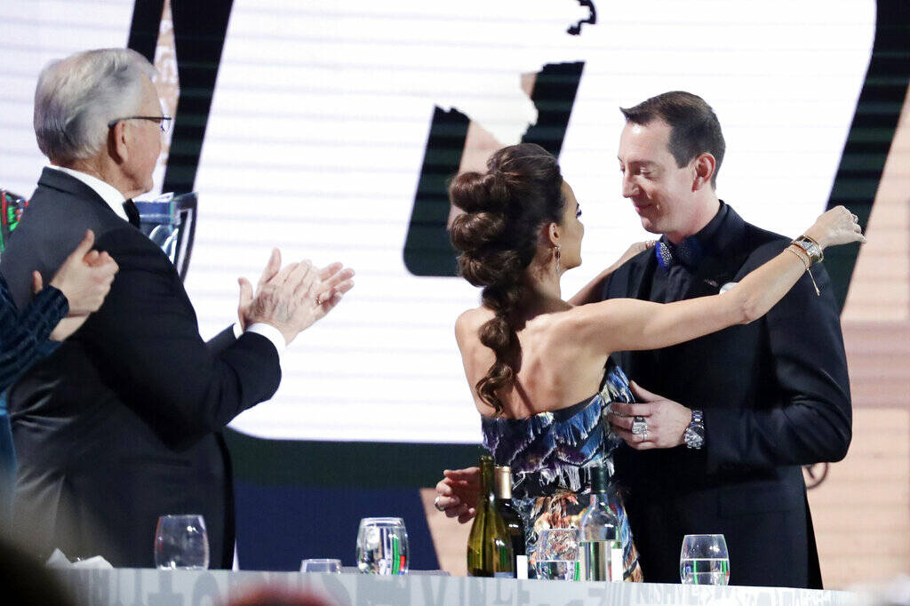 Kyle Busch, right, is hugged by his wife, Samantha, and applauded by team owner Joe Gibbs, left ...