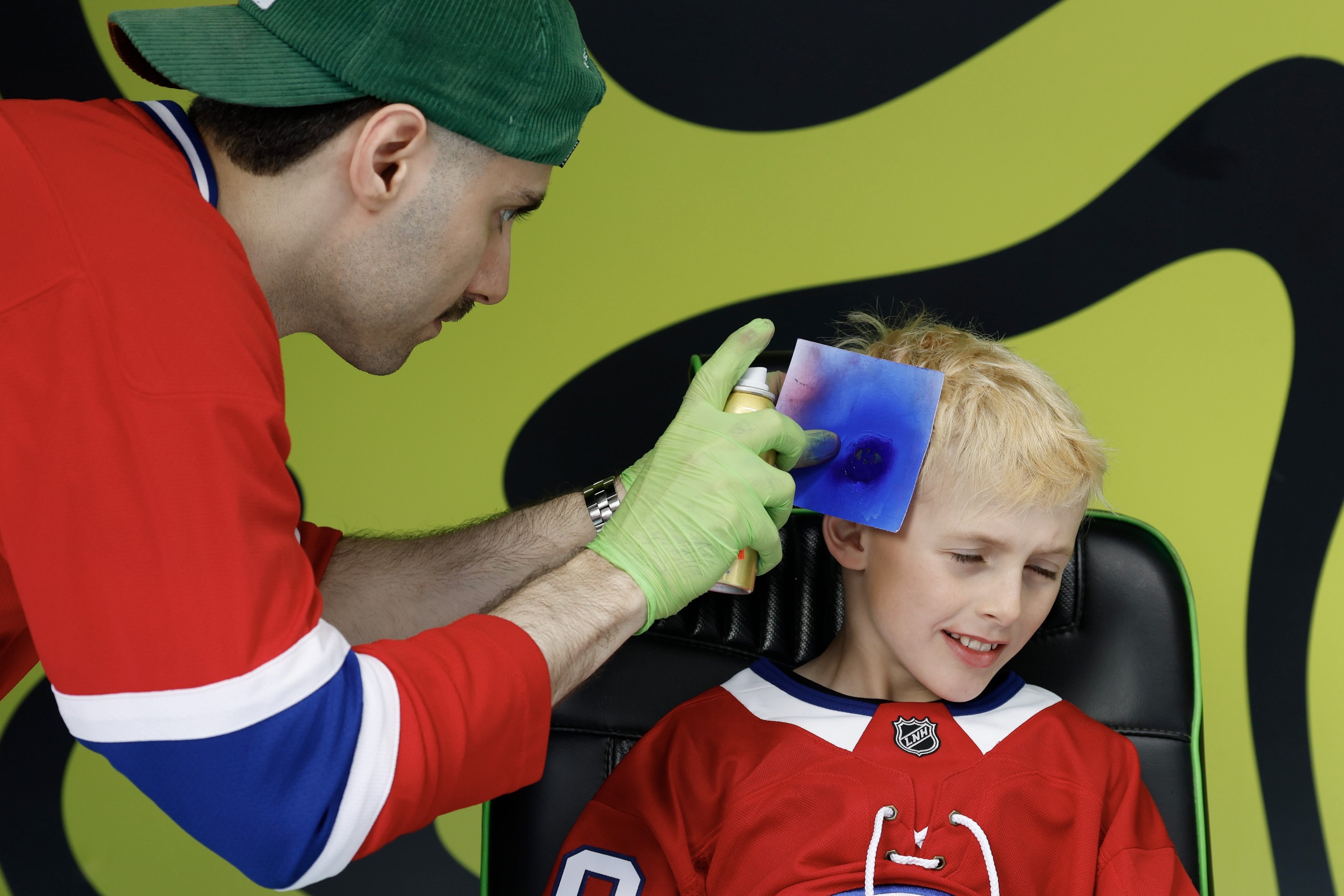 Child in Canadiens jersey having logo spray painted onto his head by man in Canadiens jersey