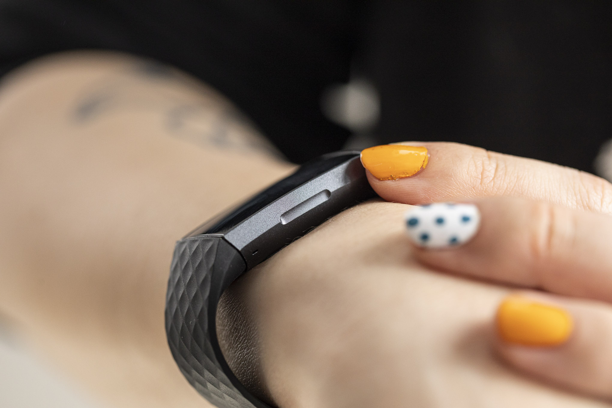 Person with colorful manicure using the Fitbit Charge 3 with a clear view of the inductive button.