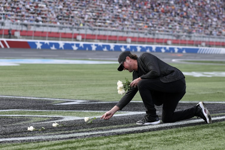 A man laying white flowers down on astroturf at a racetrack.
