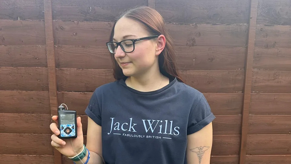 A woman in a blue Jack Wills T-shirt looks down at a pump device she is holding in her right hand.
