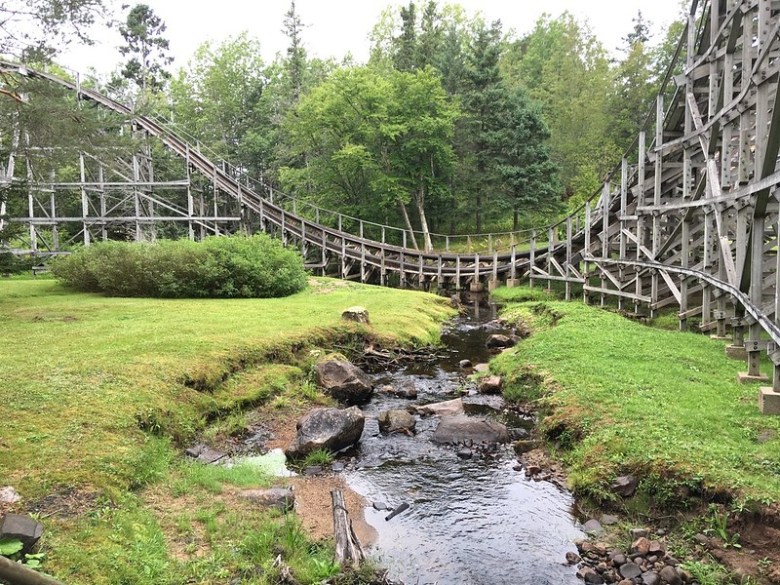 A wooden roller coaster in the mist, with part of the track passing over a creek.