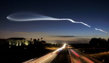 a streak of white gas stretches across a nearly dark twilight sky above a freeway lined with palm trees