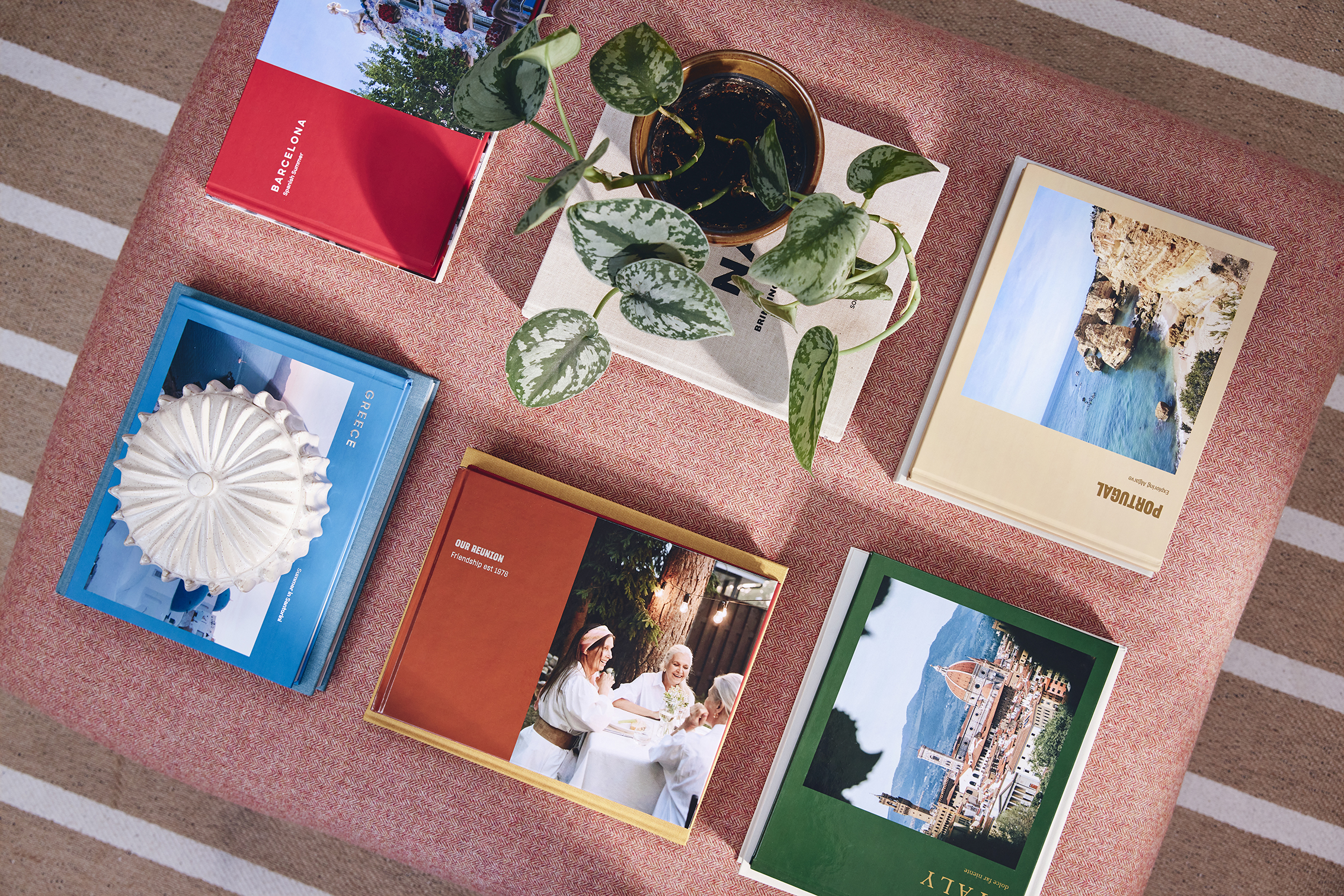 Top-down view of a pink table with six photo books, a potted plant, and a decorative object on a blue book
