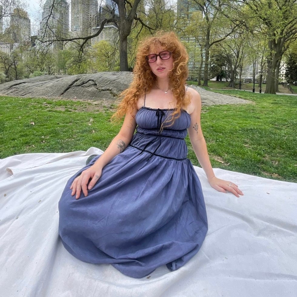 A person sitting on a blanket in a park with skyscrapers in the background.