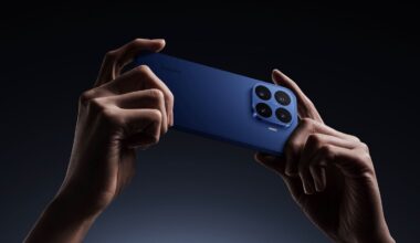 Two hands hold a blue smartphone horizontally against a dark background, showing the large quad-camera module on the back and the Xiaomi logo.