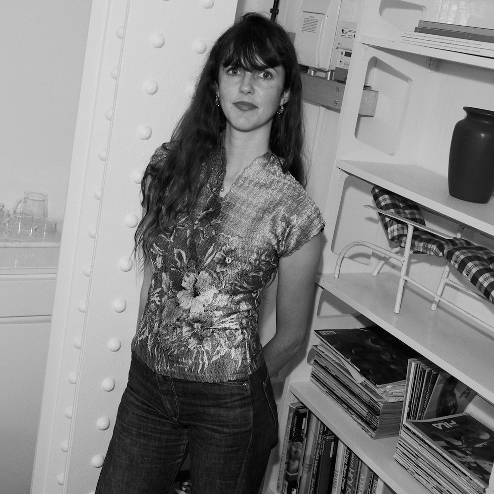 Person leaning against a white pillar with a bookshelf in the background.