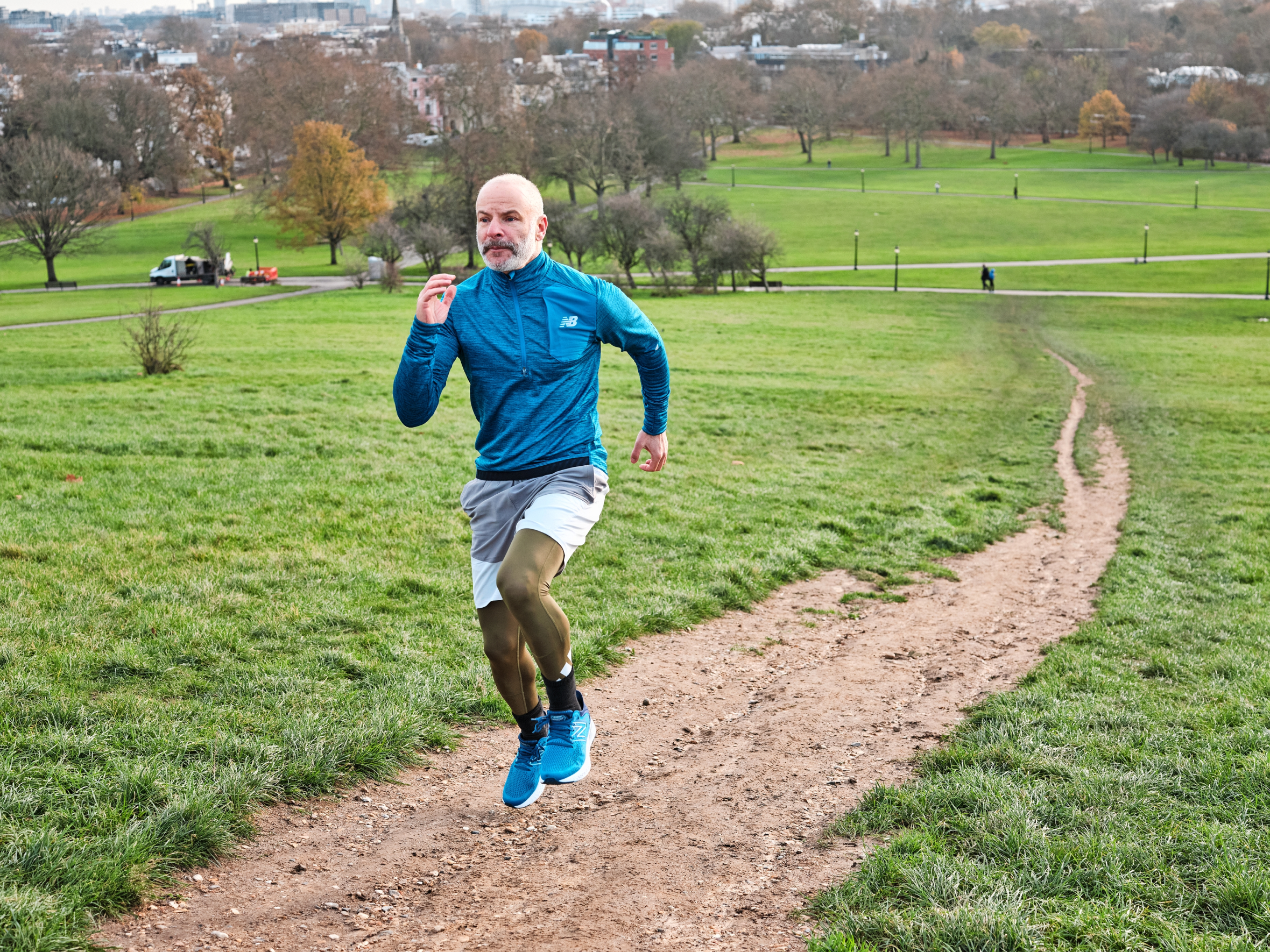 Phil Hilton running on a dirt path in a park with green grass and trees in the background.
