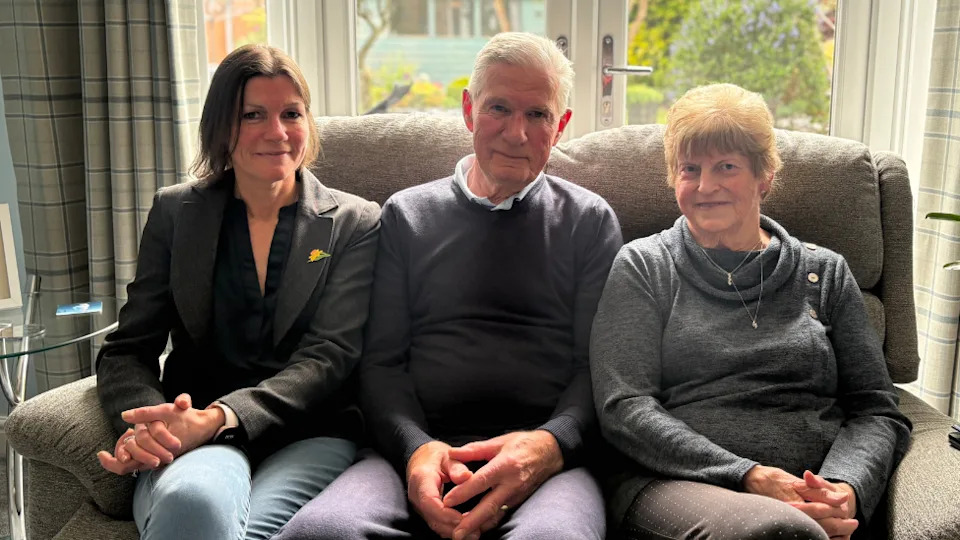 Three people - a woman, a man and another woman, sat on a sofa in front of glass doors