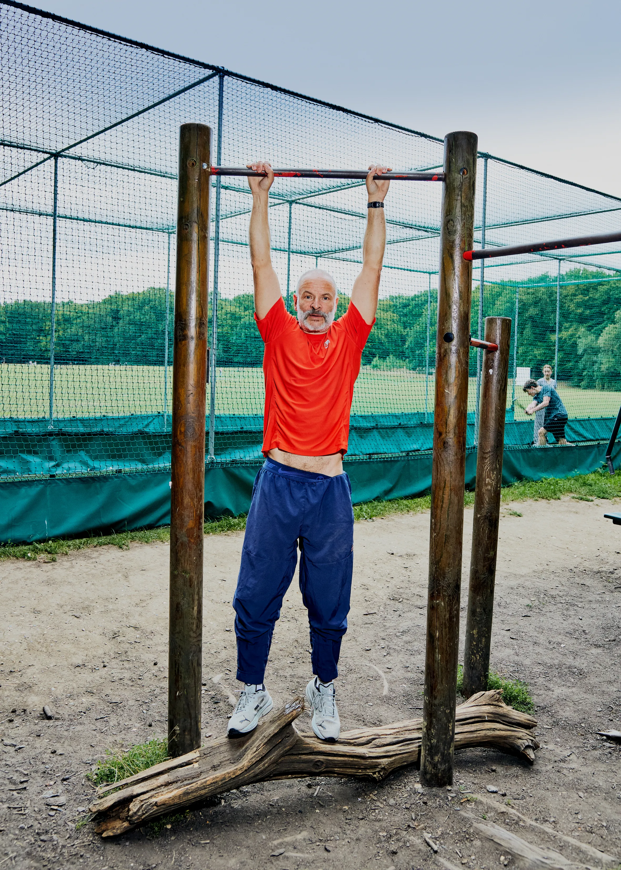 Phil Hiton doing a fitness challenge, hanging from a pull-up bar with his feet resting on a log.