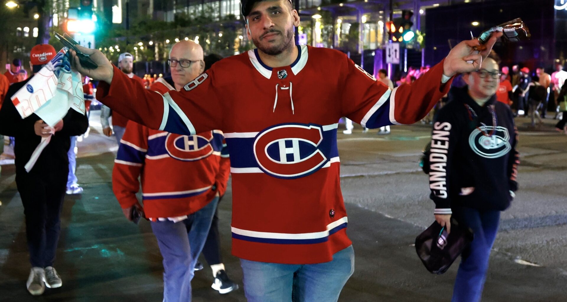 A man in a Canadiens jersey shrugs as he crosses the street at night.