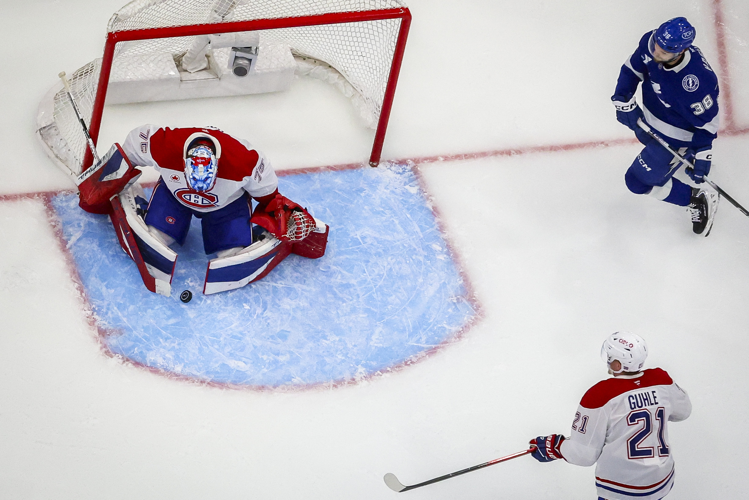 Montreal Canadiens goaltender Jakub Dobes looks at the puck as Tampa Bay Lightning left wing Brandon Hagel and Canadiens defenceman Kaiden Guhle look on